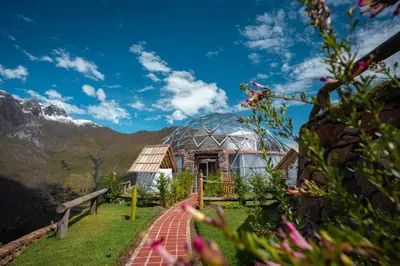 a glass house in a garden with mountains in the background at Stardome Spiritual Experience in Ollantaytambo