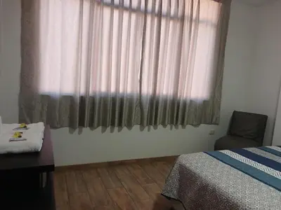a bedroom with a bed and a window with a chair at Hospedaje Margarita in La Merced