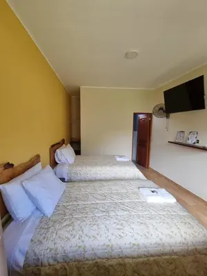 two beds in a hotel room with a tv on the wall at Pampa Bella Lodge in La Merced