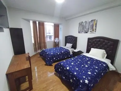 a hotel room with two beds and a table at Hostal Pacífico Huánuco in Huánuco