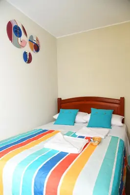 a bed with a colorful striped blanket and blue pillows at Departamento Hermoso en Residencial - Huacachina in Ica