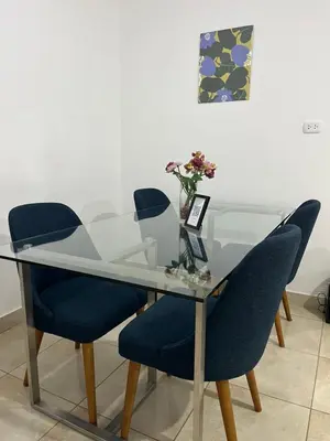 a glass table with blue chairs and a vase of flowers at MH Apartments Ica in Ica