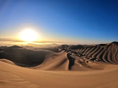 a desert scene with the sun setting in the horizon at Duna Camp Huacachina in Ica
