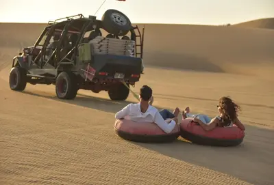 a man and woman riding on bean bags in the desert at Duna Camp Huacachina in Ica