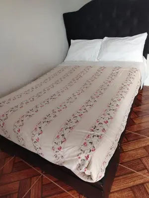 a bed with a white comforter on top of it at Hospedaje Olguita in Oxapampa