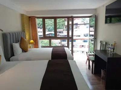 a hotel room with two beds and a desk and a window at Hotel Pucara Machupicchu in Machu Picchu