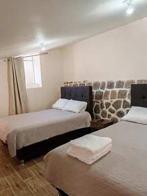 a room with two beds and a stone wall at Centro Cusco Inti in Cusco