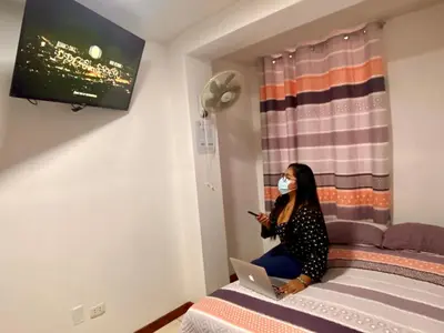 a woman wearing a mask sitting on a bed with a laptop at Hostal Venus - Nueva Imagen in Huacho